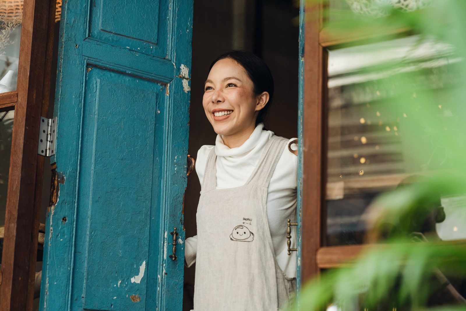 A smiling café owner in an apron stands in the doorway of her own shop