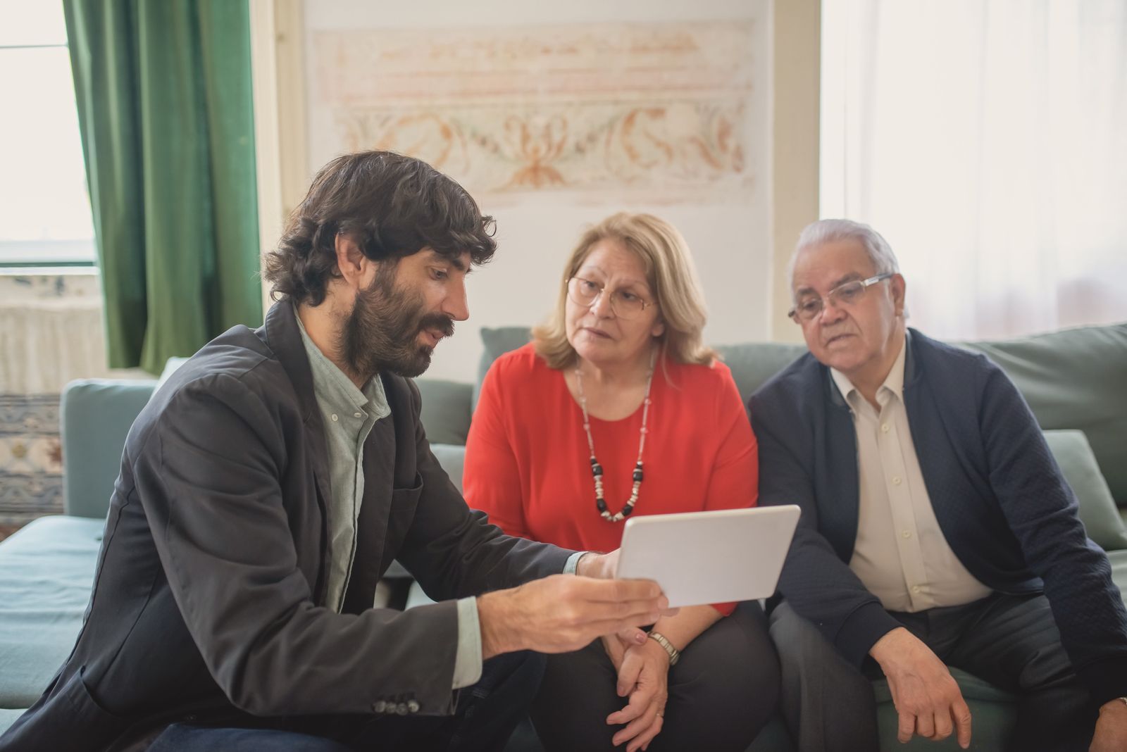 An advisor walks a mature couple through plan figures on a tablet in a bright living room
